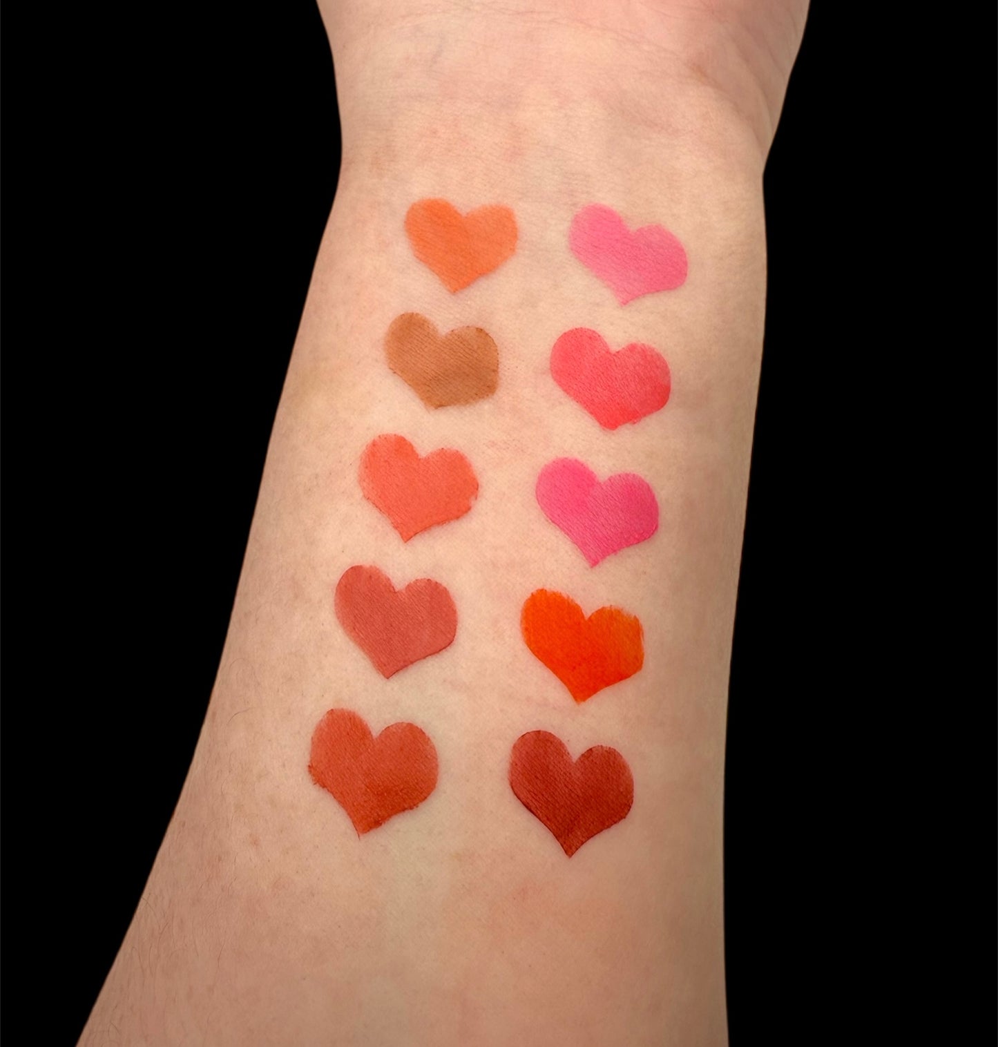 Heart-shaped blush swatches on a person's arm with a black background
