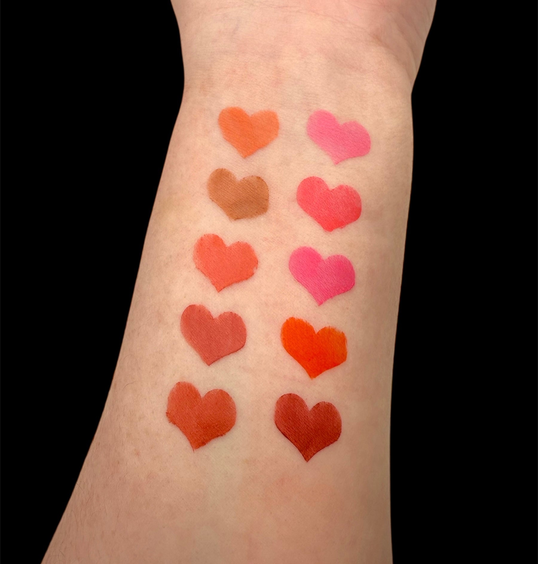 Heart-shaped blush swatches on a person's arm with a black background 