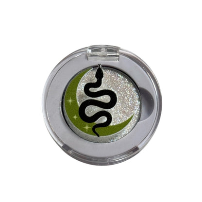Round metallic object with a black snake design on a green circle, on a white background
