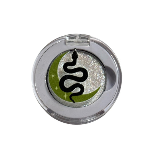 Round metallic object with a black snake design on a green circle, on a white background